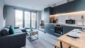 A modern kitchen with dark cabinets, a microwave, and a dining area with a table set for two. - Stylish City Centre Apartment (Leeds)