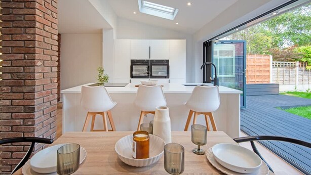 Een moderne keuken met witte kastjes, een centraal eiland en een eetgedeelte met een houten tafel en stoelen.