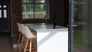 Een moderne keuken met een centraal eiland, houten krukken en een glazen deur naar een buitenruimte.
