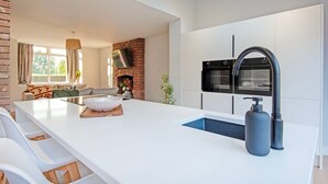Een moderne keuken met een centraal eiland, witte kasten, een ingebouwde oven en een grote kraan.