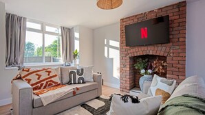 Een woonkamer met een bank, een aan een bakstenen muur bevestigde televisie, en een raam met gordijnen.