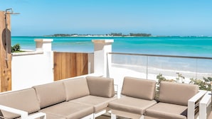 Un balcón con dos sofás color beige, un portón de madera y vistas a la playa y al océano.