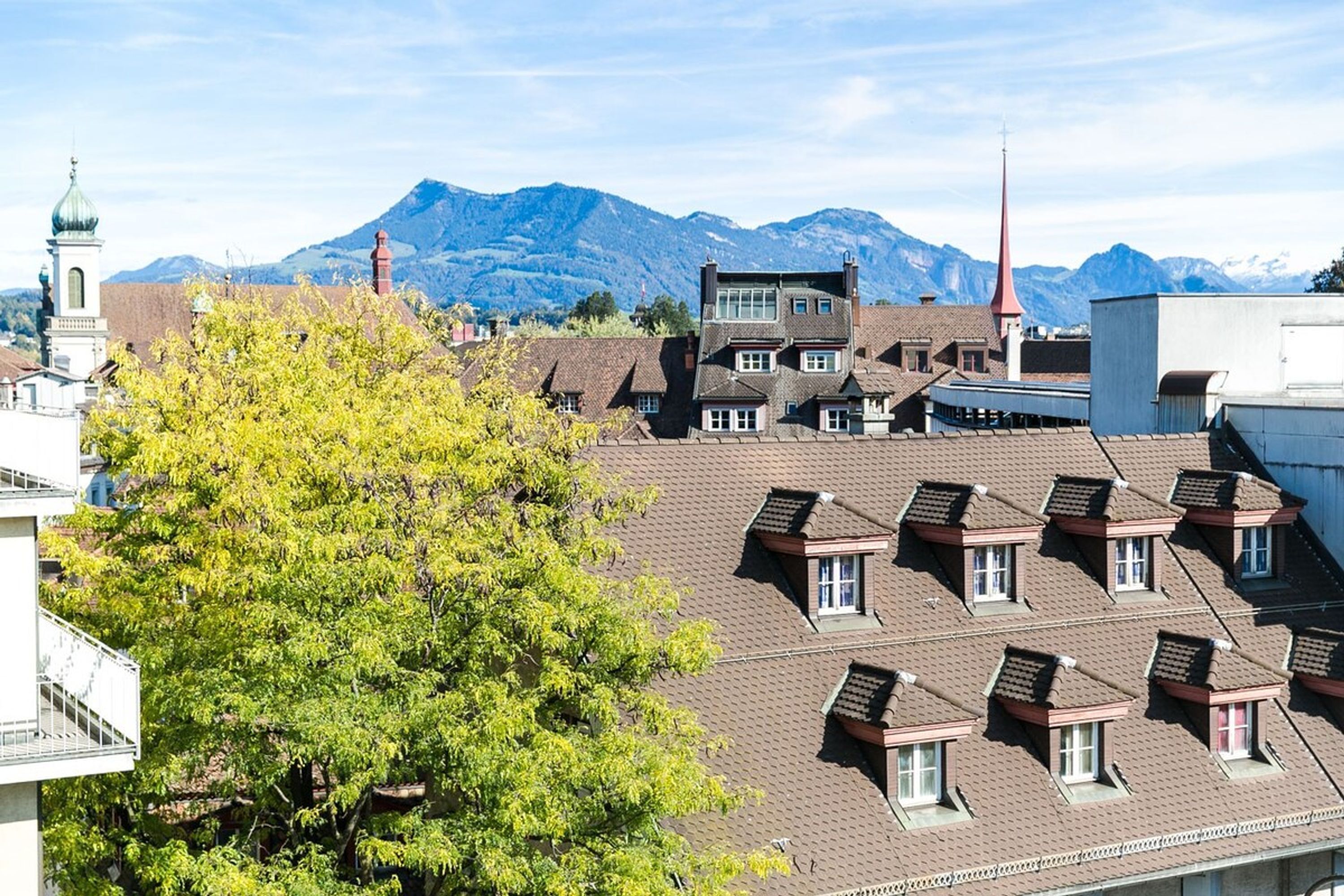A residential area with multiple buildings, including a prominent church with a tall spire, and a mountain range in the background.