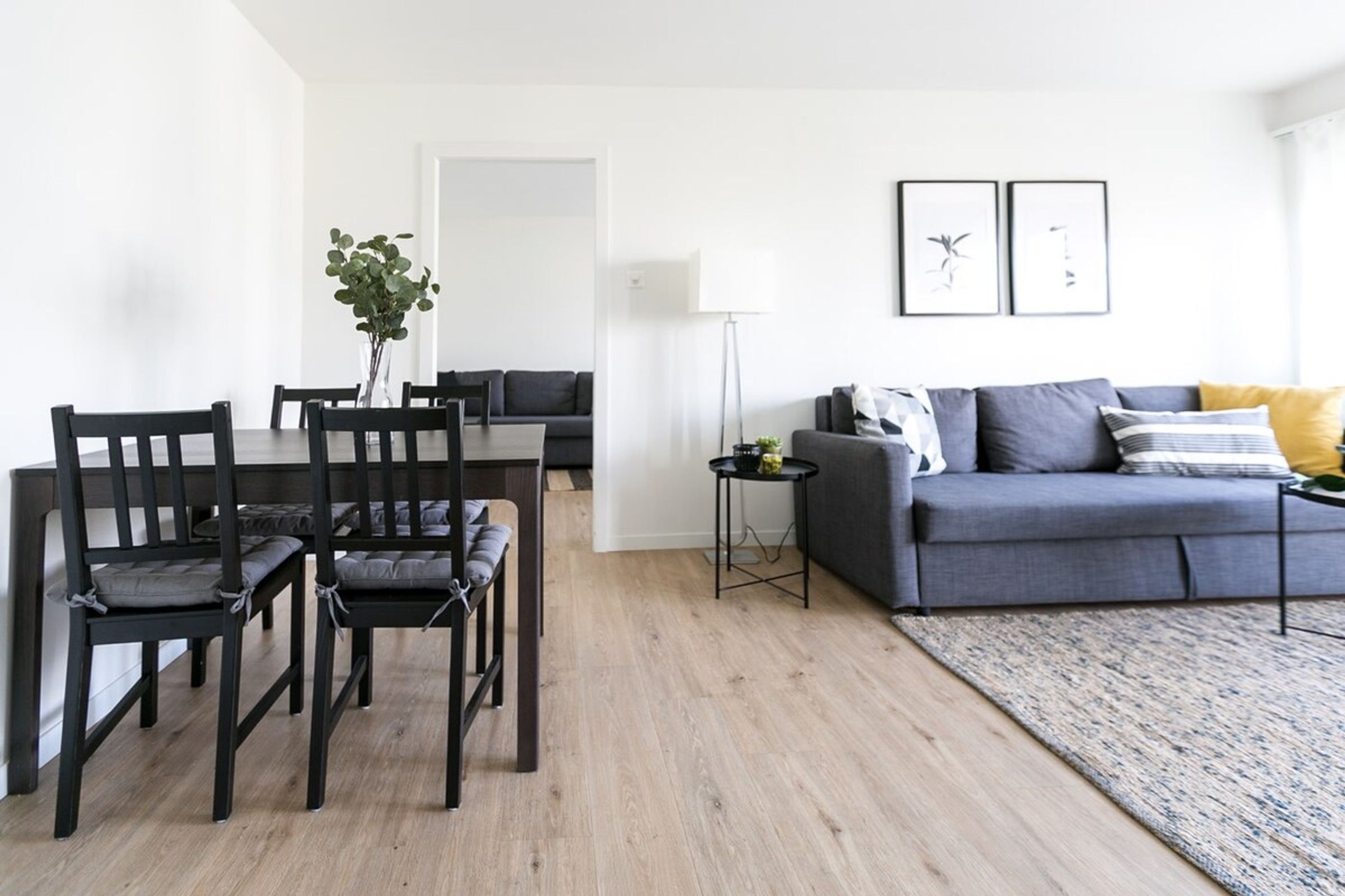 Una sala de estar moderna con comedor, que incluye un sofá gris, sillas negras y una mesita auxiliar.