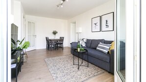 A modern living room with a grey sofa, a coffee table, a dining table with chairs, and a large window. - Modern Flat w Netflix Balcony top Location (Lucerne)