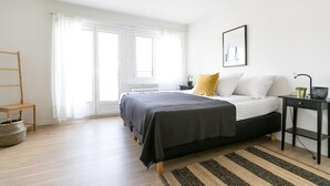 A bedroom with a bed, a bedside table, a lamp, a chair, and a window with curtains. - Modern Flat w Netflix Balcony top Location (Lucerne)