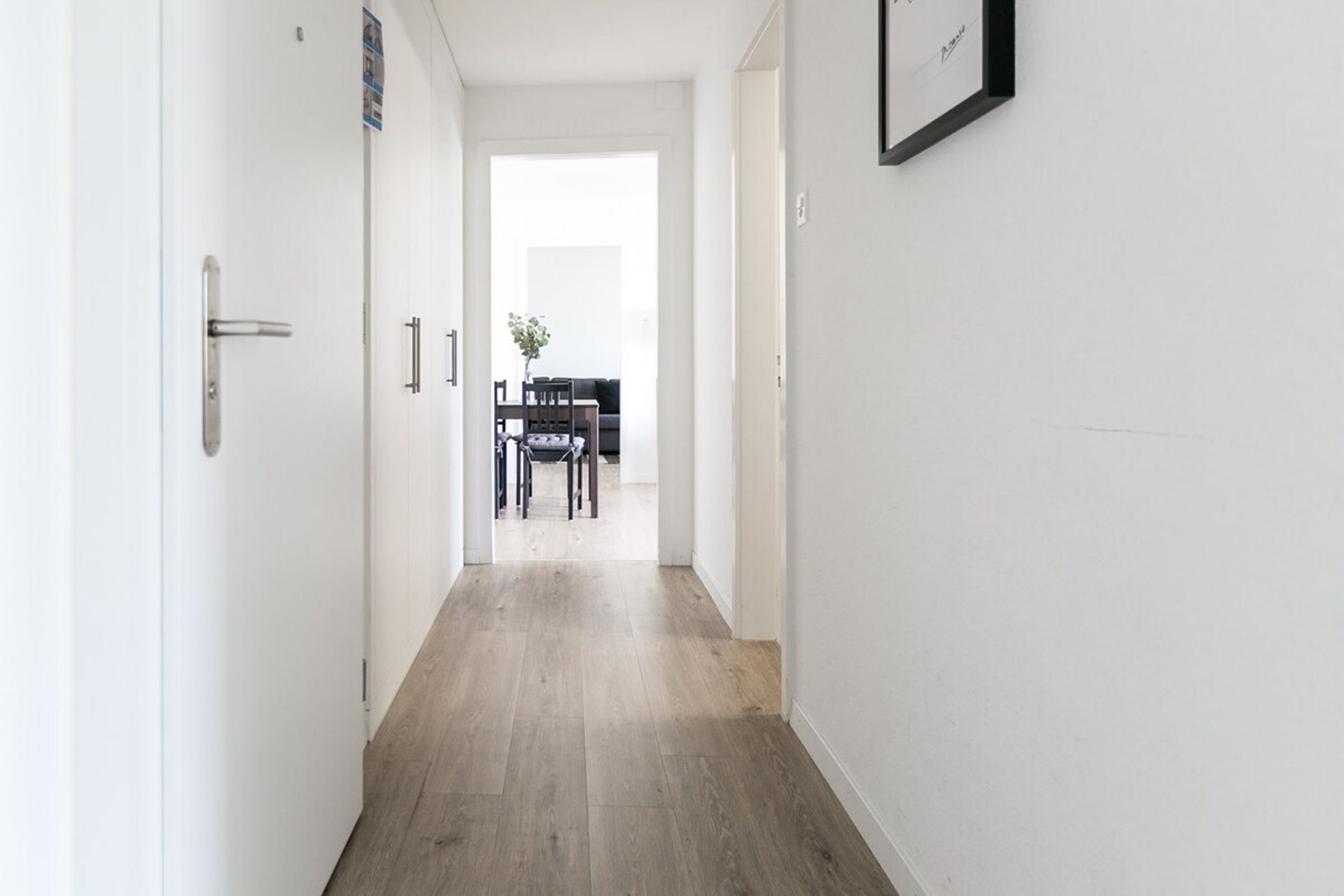 Un corridoio stretto con pavimento in legno che conduce a una sala da pranzo con tavolo e sedie.