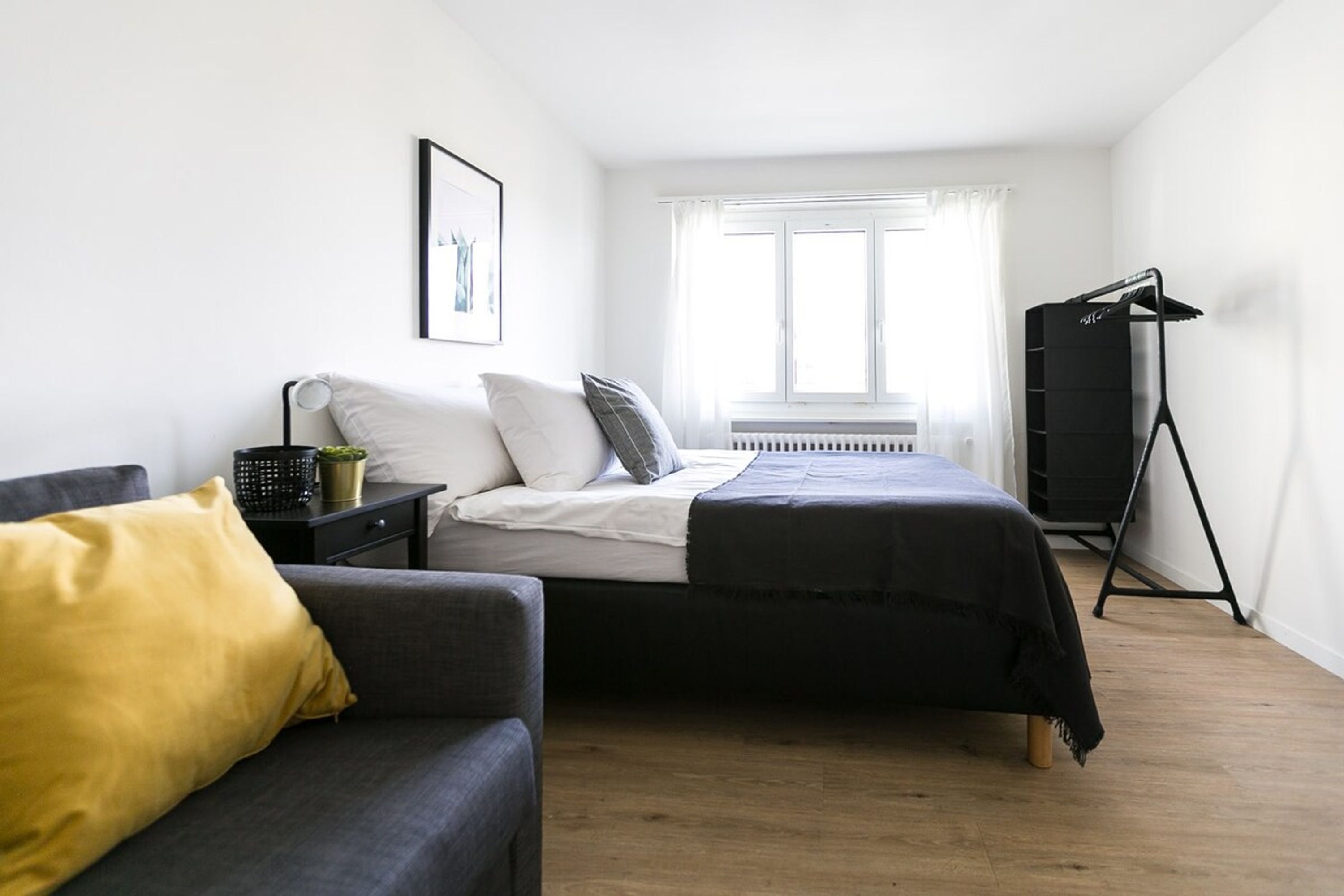 A bedroom with a bed, a sofa, a radiator, a window, and a black wardrobe.