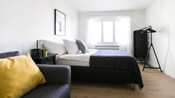 A bedroom with a bed, a sofa, a radiator, a window, and a black wardrobe.