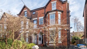 A two-story brick house with a front entrance, a small porch, and a garden area with plants and a stone feature. - Cosy Apartment in Stunning Didsbury (Manchester)
