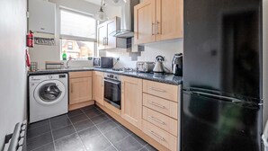 A modern kitchen with wooden cabinets, a black refrigerator, a washing machine, and a stove. - Cosy Apartment in Stunning Didsbury (Manchester)