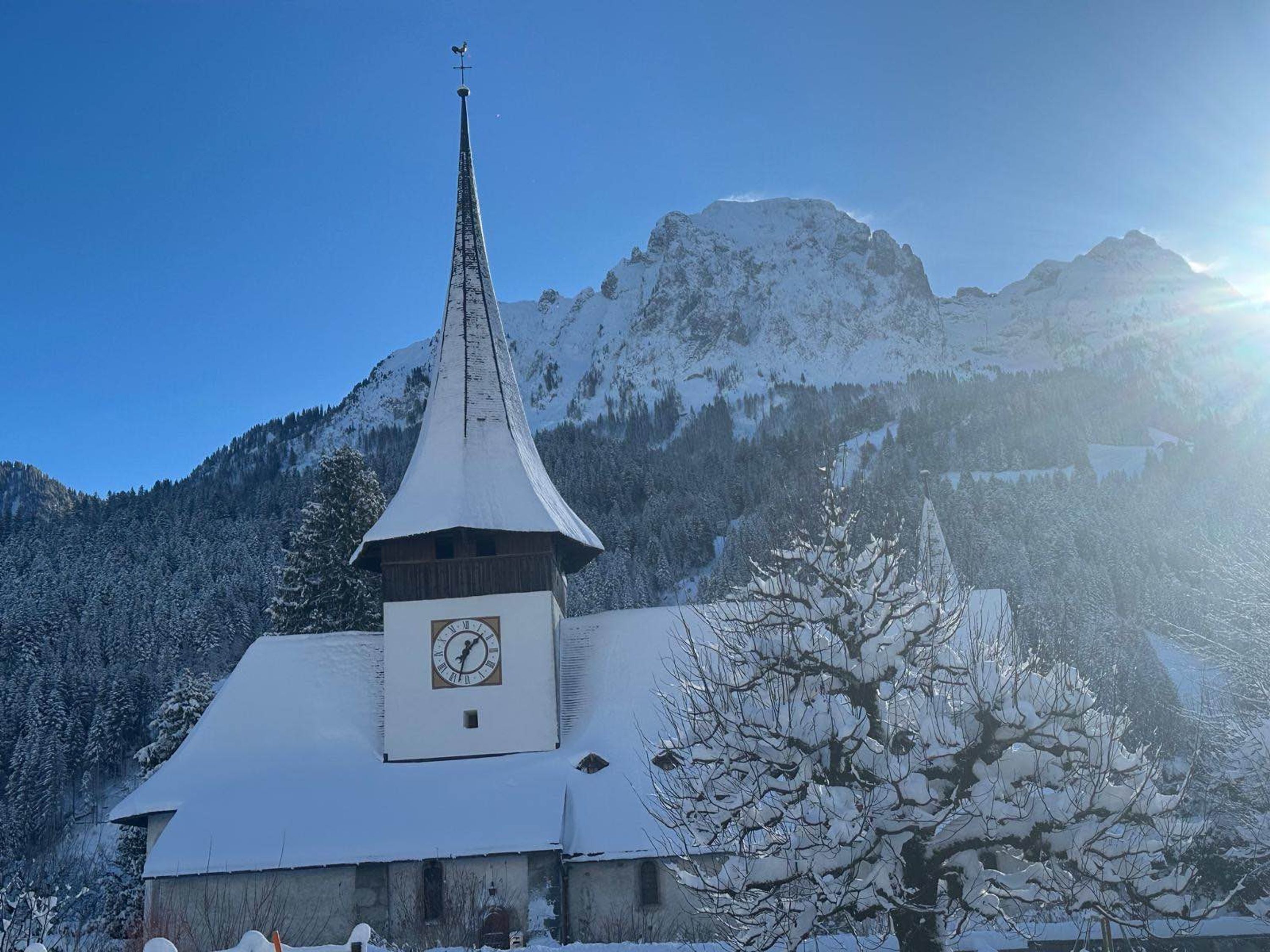 A church with a clock tower, surrounded by snow-covered mountains.