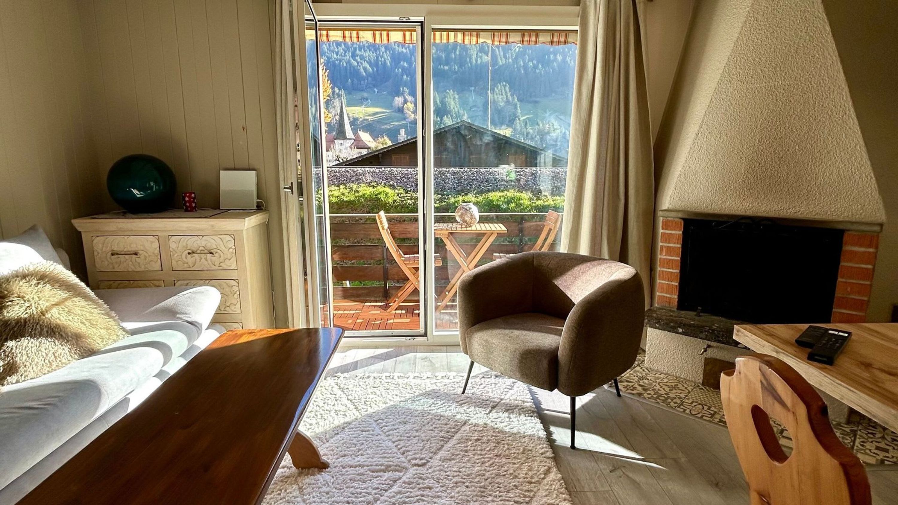Ein Schlafzimmer mit einer großen Schiebeglasdoor, die auf einen Balkon führt, einem Kamin, einem Holztisch und einem gemütlichen Sessel.