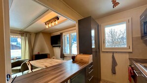 A compact kitchen with a wooden table, a built-in oven, a microwave, and a window with a view of trees. - Le Petite Chalet in Rougemont (Rougemont)