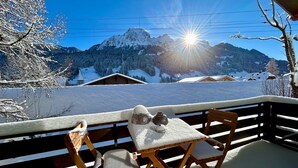 A wooden deck with a table and chairs, overlooking a snowy mountain landscape with a clear sky and a bright sun. - Le Petite Chalet in Rougemont (Rougemont)