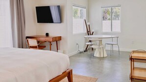 Un dormitorio con cama, escritorio, televisor, mesa de comedor con sillas y carrito.