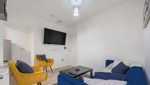 Una sala de estar moderna con un sofá, dos sillones amarillos, una mesa de centro y un televisor de pantalla plana montado en la pared.