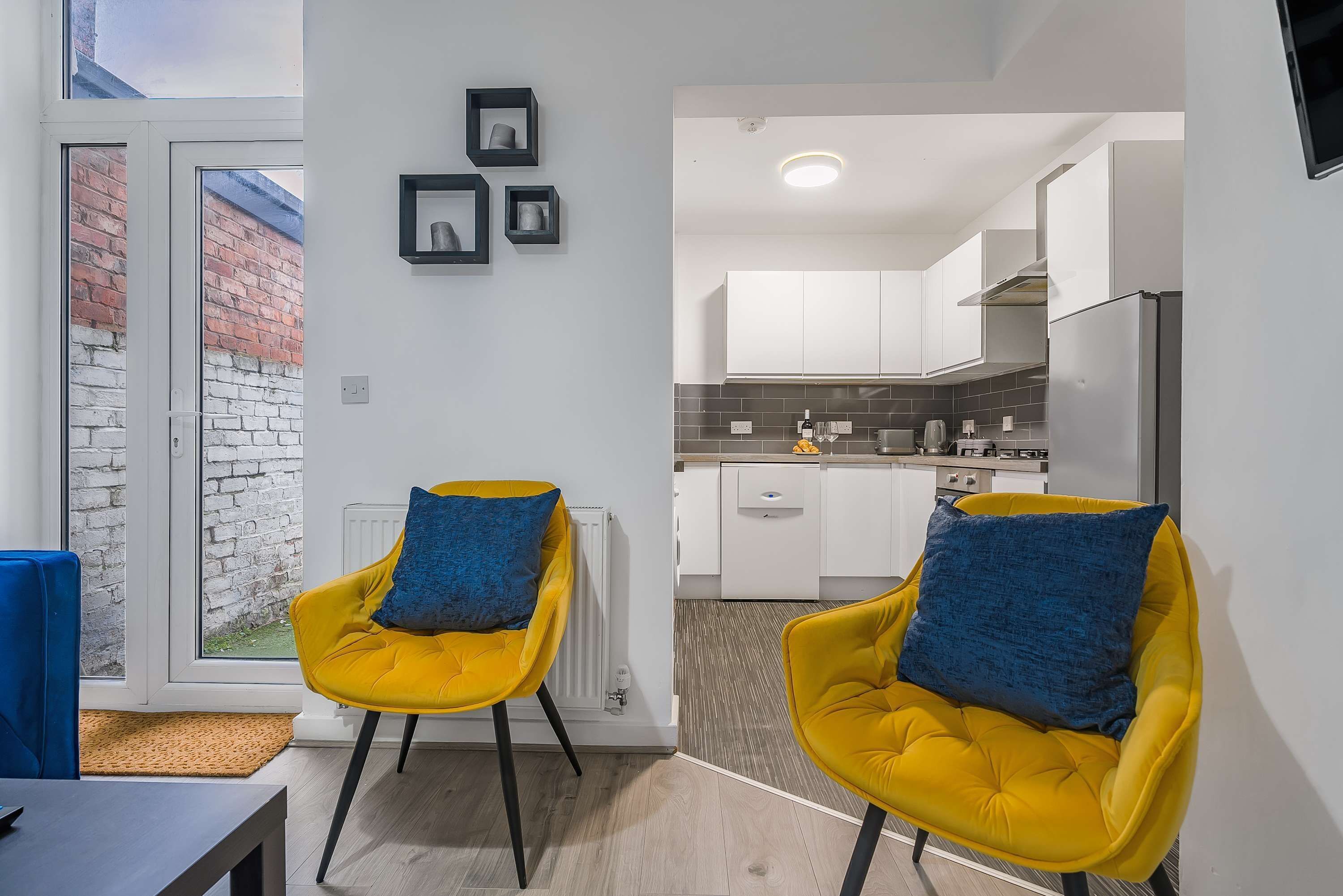 Um apartamento moderno com duas cadeiras amarelas, uma mesa de jantar e uma cozinha com armários brancos.