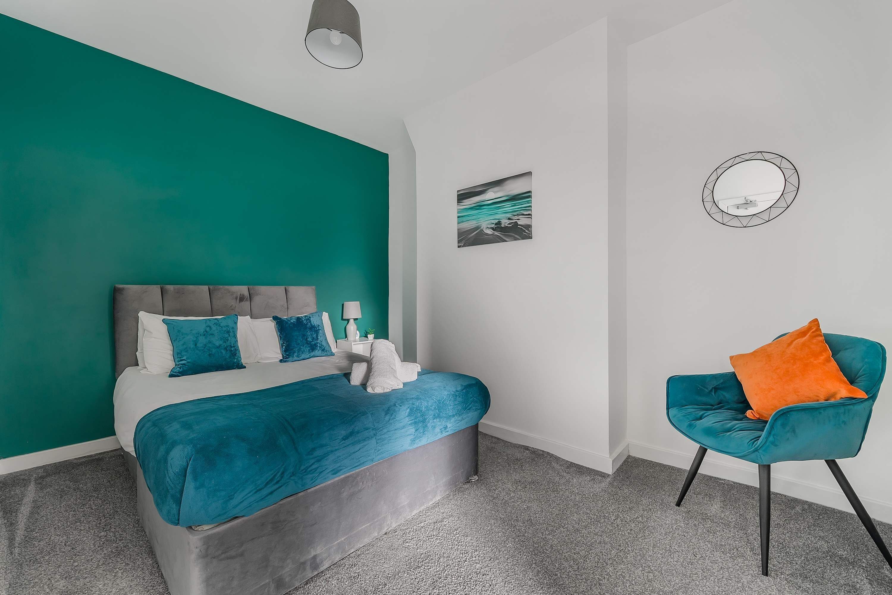 A bedroom with a bed, a chair, a wall with a painting, and a mirror.