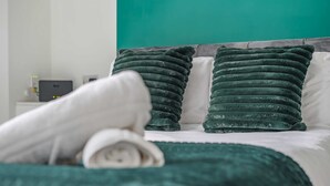 Una cama con un edredón y almohadas color aguamarina, un cabecero blanco y una mesita de noche con una lámpara.