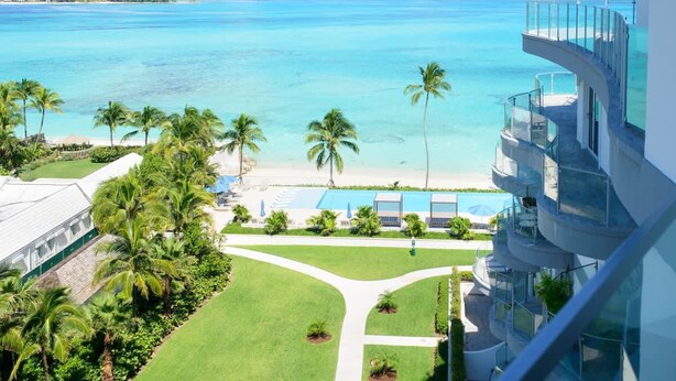 A hotel with a pool, palm trees, and a view of the ocean. - 2 Bed Ocean View Condo at ONE Cable Beach (Nassau)