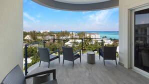 A balcony with wicker furniture, a round table, and a view of the ocean and buildings. - 2 Bed Ocean View Condo at ONE Cable Beach (Nassau)