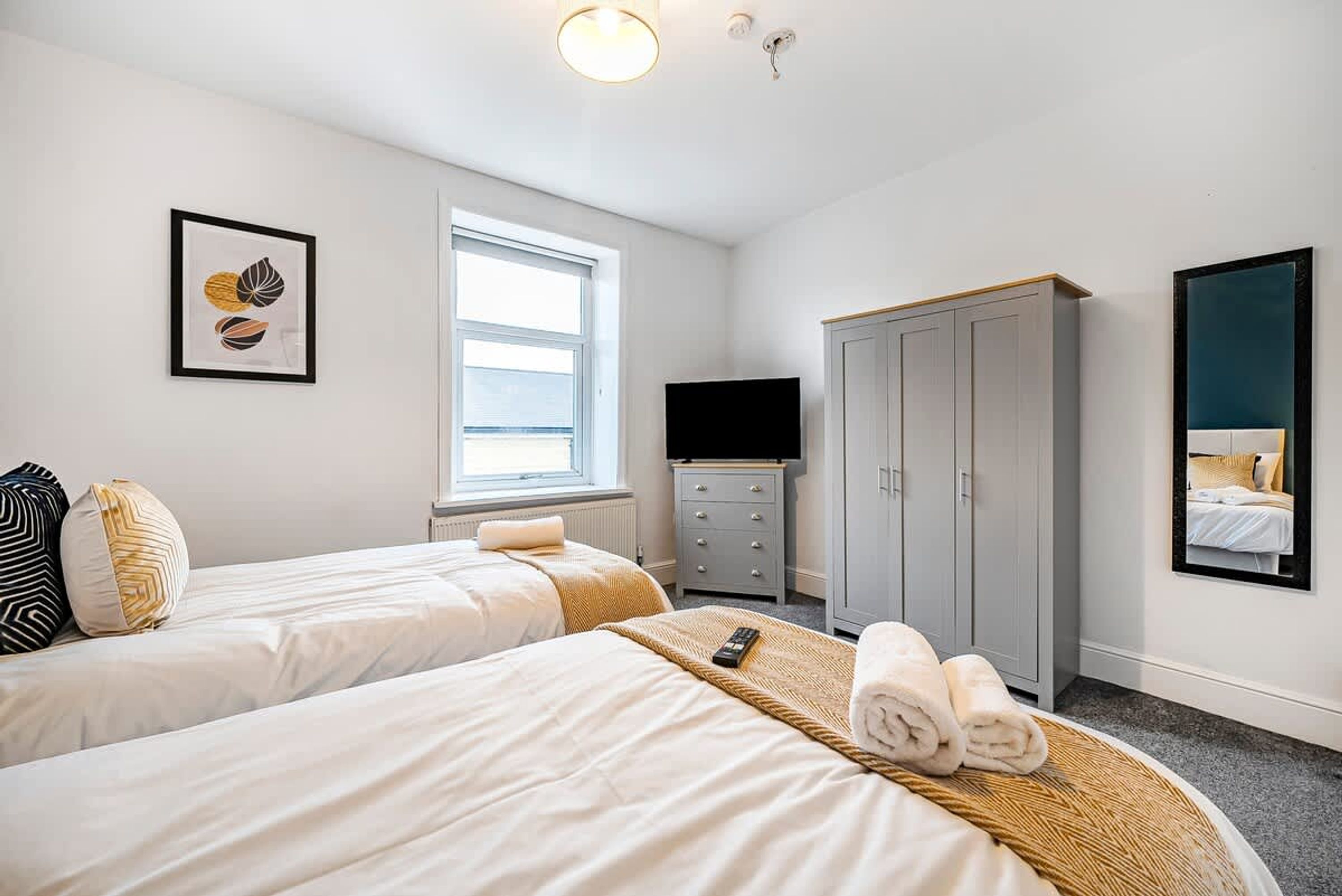 Quarto de hotel com duas camas, um guarda-roupa, uma televisão e uma janela.