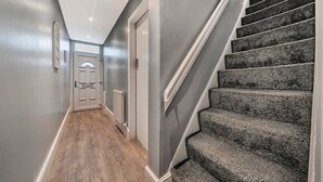 A hallway with a wooden floor, a grey wall, and a staircase with grey carpeted steps.