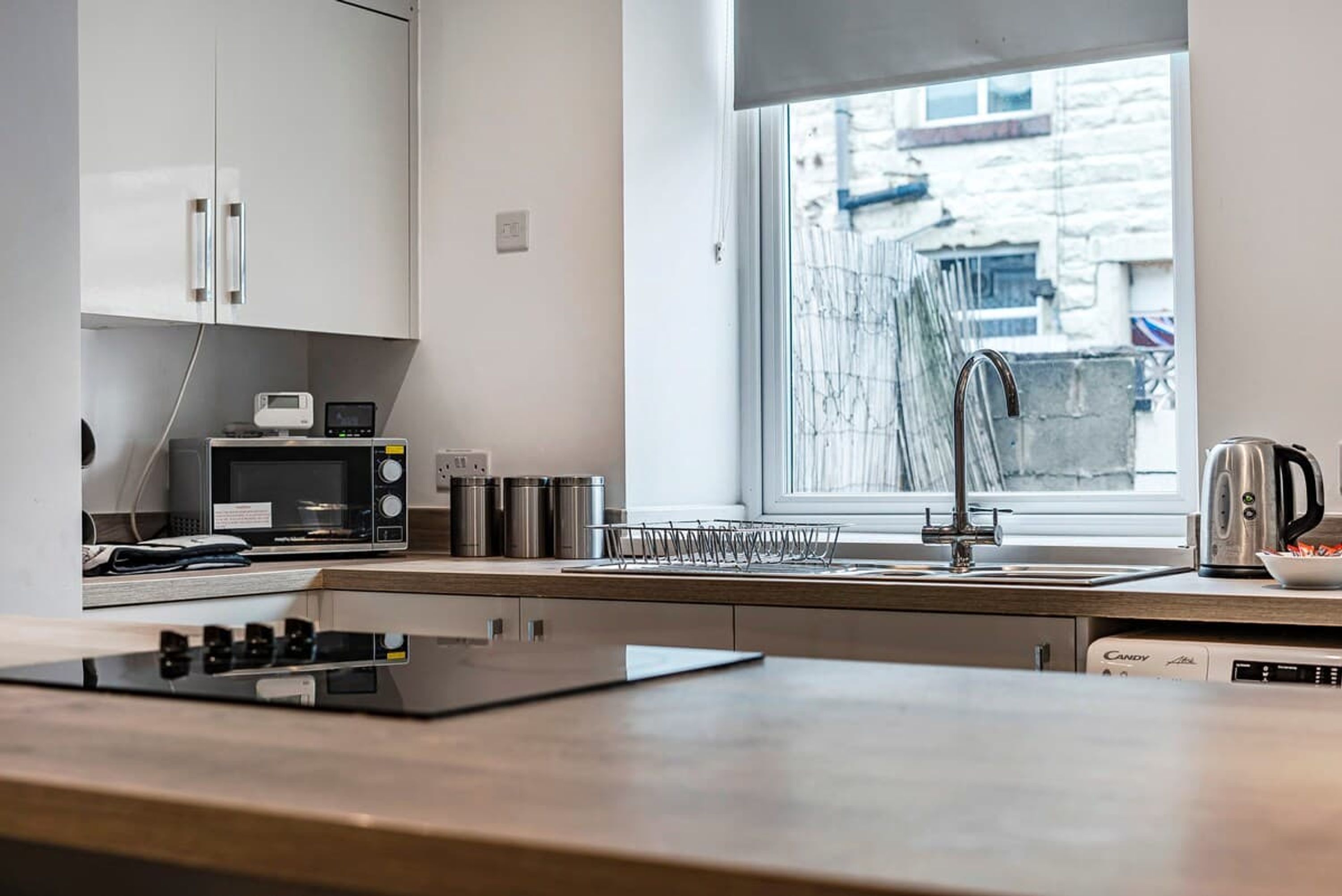 Una cocina moderna con armarios blancos, microondas, hervidor y lavavajillas.