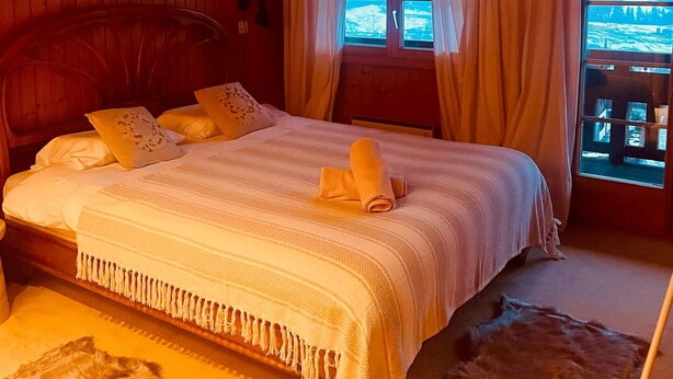 Una habitación acogedora con una cama de madera, un ventanal con cortinas y vistas a un paisaje nevado.