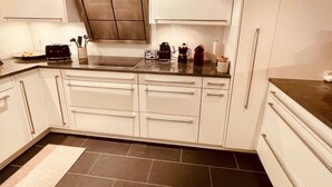 Una cocina moderna con armarios blancos, extractor de acero inoxidable y encimera negra.