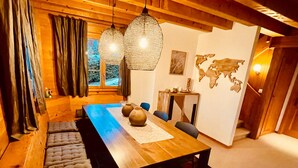 Un comedor acogedor con una larga mesa de madera, asientos tipo banca con cojines e iluminación colgante de fibra.