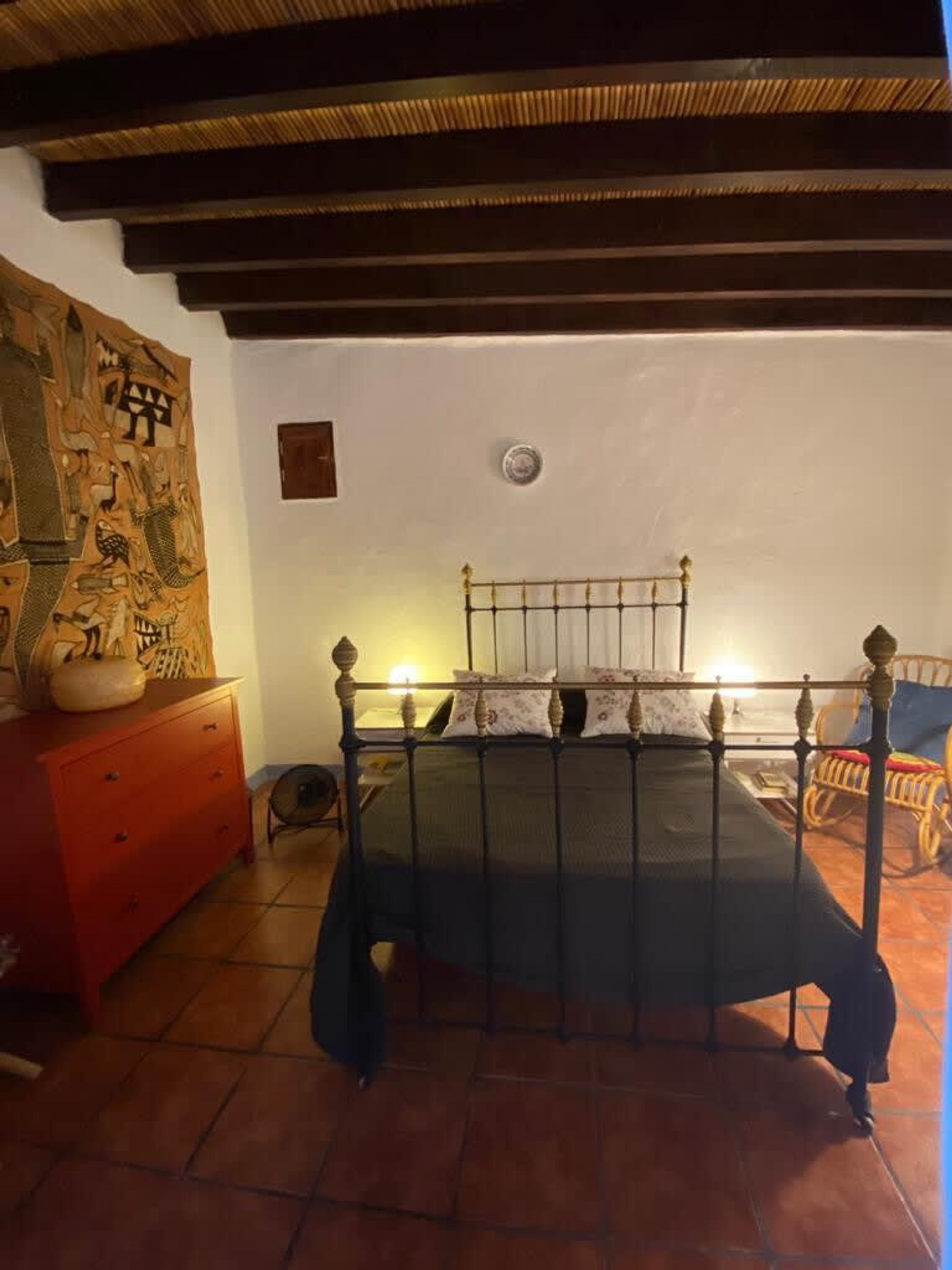 Un dormitori amb llit, tocador, cadira i un mur amb una tapestry.