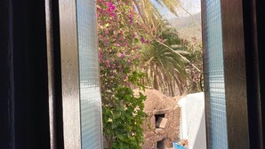 A doorway leading to a courtyard with a stone structure, lush greenery, and a palm tree. - 4BR Heaven Close to Nature and Ocean in Quiet Setting (Agaete)