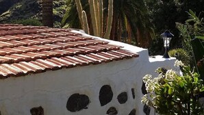 A white building with a tiled roof and a wall with circular cutouts, surrounded by cacti and palm trees, with a mountainous backdrop. - 4BR Heaven Close to Nature and Ocean in Quiet Setting (Agaete)