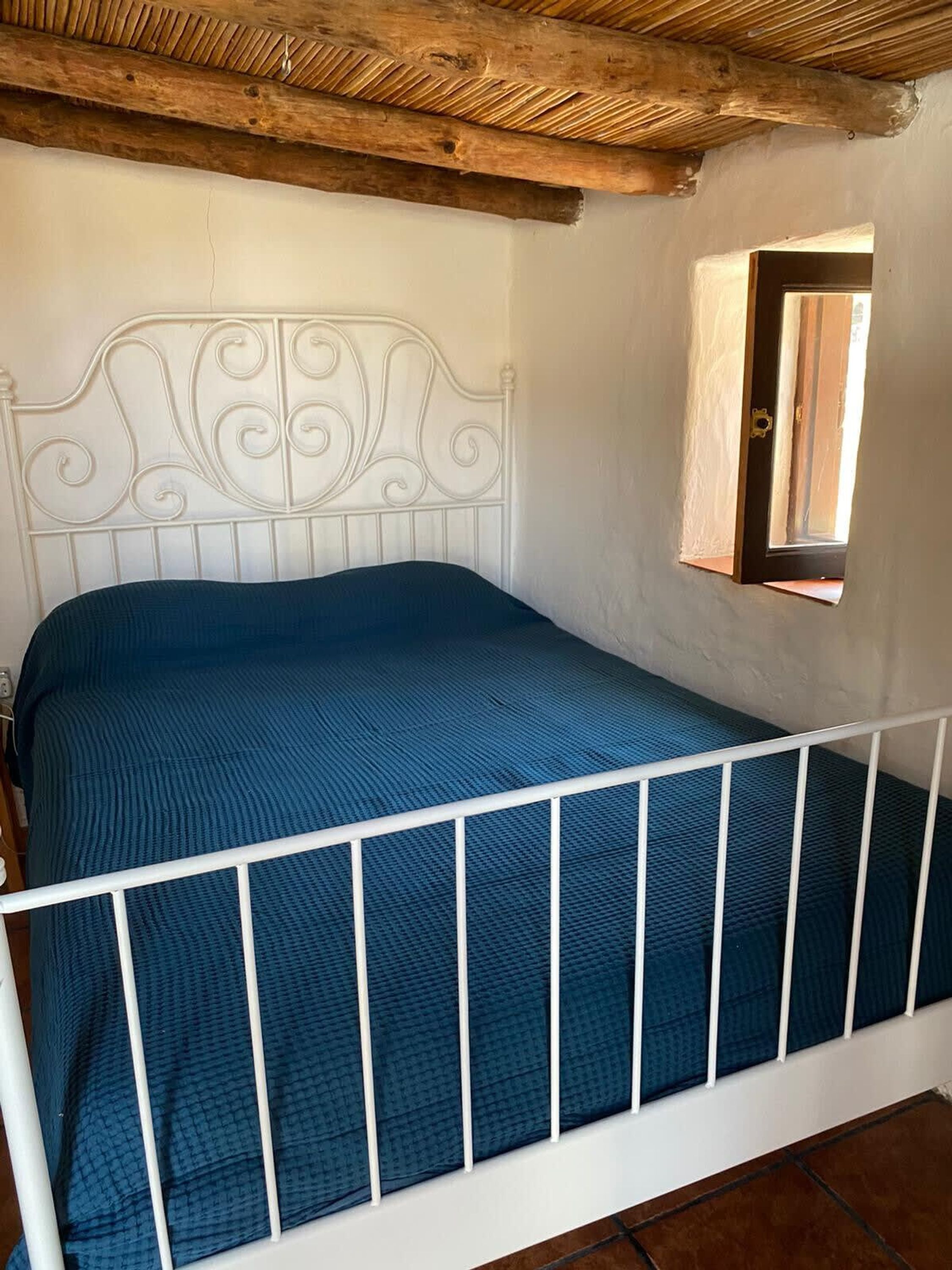 A bedroom with a white metal bed frame, a blue mattress, and a wooden ceiling.