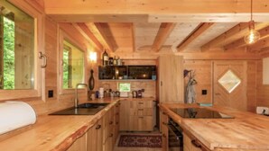 A compact wooden kitchen with a central island, built-in cabinets, and a window overlooking greenery. - Alps Chalet for Big Group With Sauna Yoga Terrace (Rossiniere)