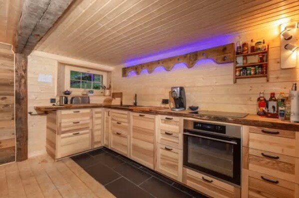 A wooden interior with a kitchen area, including cabinets, a stove, and a coffee machine. - Alps Chalet for Big Group With Sauna Yoga Terrace (Rossiniere)