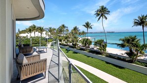 A balcony with a view of a beach, palm trees, and a pool. - Ocean Front Condo at One Cable Beach (Nassau)