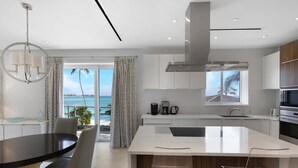 A modern kitchen with a large island, white cabinetry, and a view of the ocean. - Ocean Front Condo at One Cable Beach (Nassau)