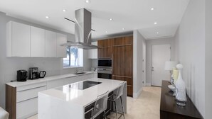 A modern kitchen with a central island, stainless steel appliances, and a mix of white and wooden cabinetry. - Ocean Front Condo at One Cable Beach (Nassau)