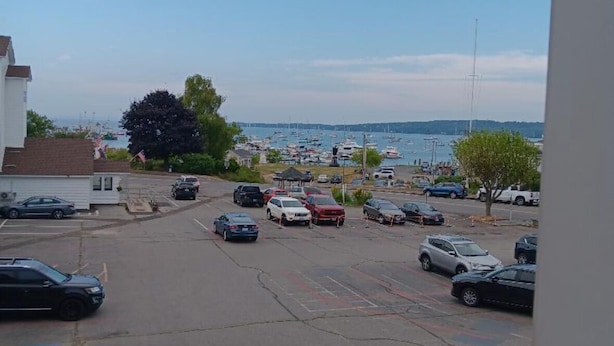 Un parking où sont garées différentes voitures, avec une vue sur une marina au loin.