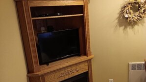 Une pièce d’angle avec un meuble de rangement en bois pour les appareils multimédias, une cheminée et une couronne décorative accrochée au mur.