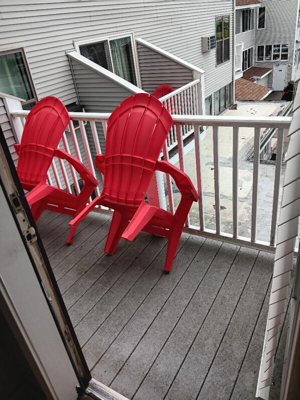 A balcony with two red Adirondack chairs, a white railing, and a view of neighboring houses.