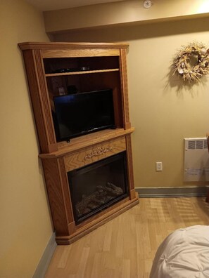 A corner room with a wooden entertainment center, a fireplace, and a wall-mounted wreath.