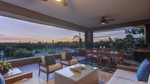 Un ampio balcone con mobili da esterno, una ventola a soffitto e vista sul tramonto.