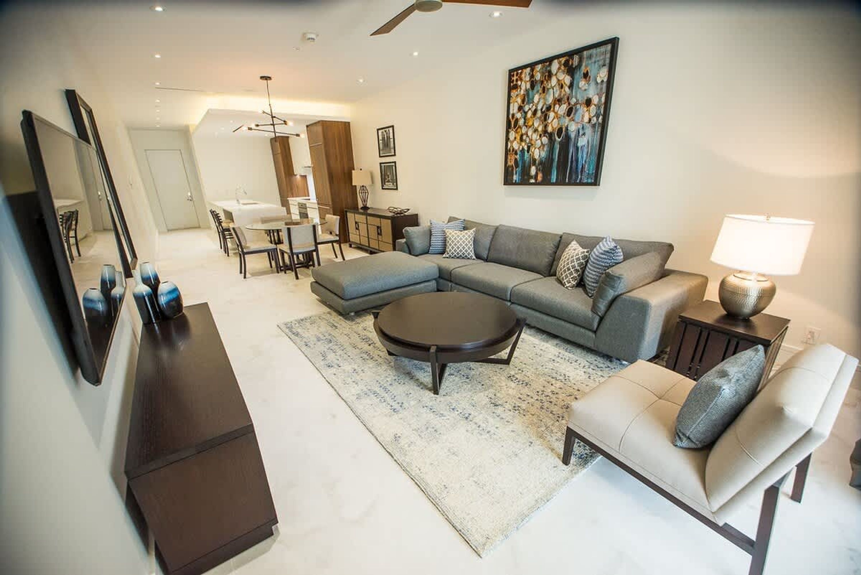 A modern living room with a sectional sofa, a round coffee table, and a dining area in the background.
