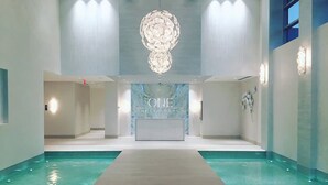 A modern hotel lobby with a central reception desk, a pool area, and a chandelier. - 2 Bed Condo at ONE Cable Beach With Balcony (Nassau)
