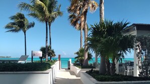 A pathway leading to a beach area with palm trees and a sign indicating no glass allowed. - 2 Bed Condo at ONE Cable Beach With Balcony (Nassau)
