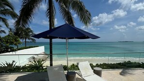 Un espace de détente aménagé sur la plage, avec deux chaises longues, un parasol bleu et un palmier.